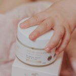 Pot de crème Tendre Bébé 50 g, une petite main de bébé posée dessus, à côté de son étui