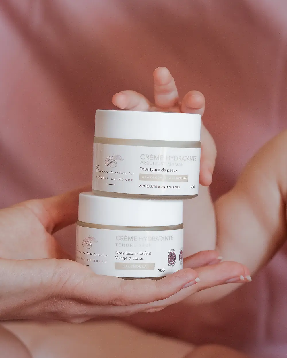 Pack douceur maternelle : les deux pots de crème empilés et tenus dans des mains